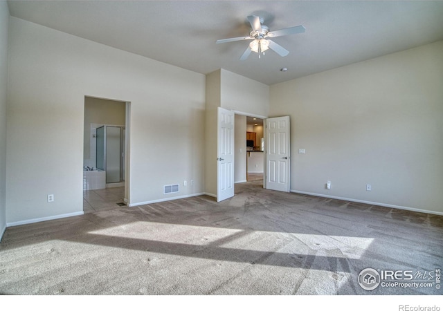 unfurnished bedroom with light colored carpet, visible vents, a towering ceiling, connected bathroom, and baseboards