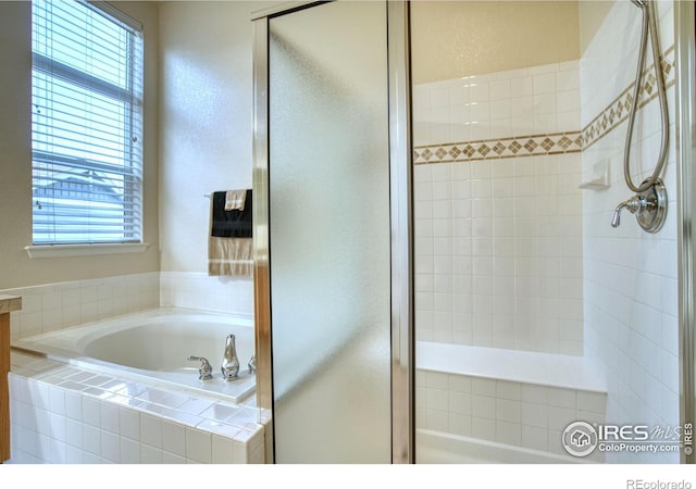 bathroom featuring a garden tub, a textured wall, and a shower stall