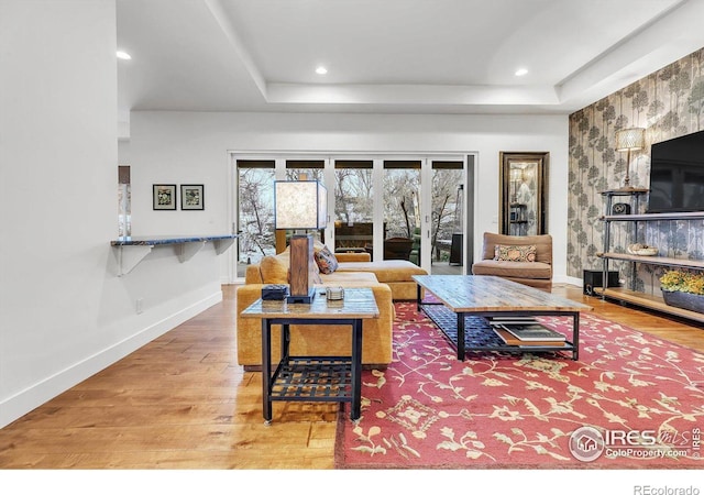 living room featuring a tray ceiling, recessed lighting, baseboards, and wood finished floors