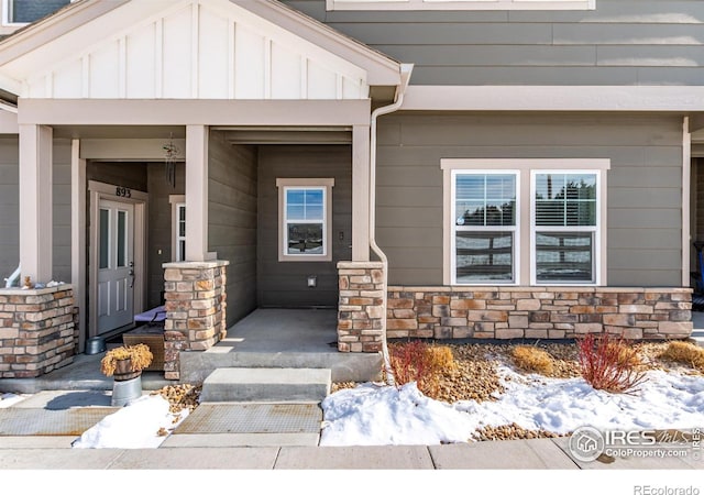 snow covered property entrance featuring board and batten siding and stone siding