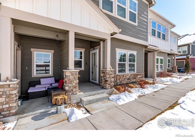 snow covered property entrance with board and batten siding and stone siding