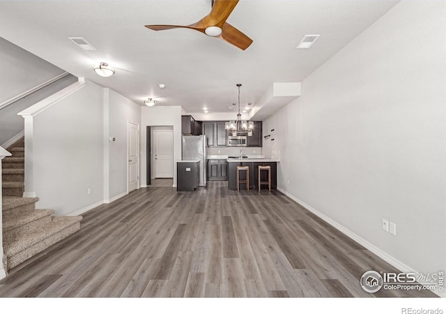 unfurnished living room featuring visible vents, dark wood finished floors, stairway, and ceiling fan with notable chandelier