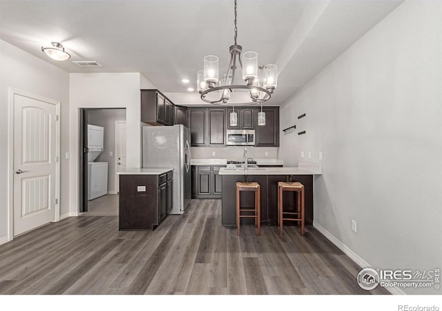 kitchen featuring visible vents, stacked washer / drying machine, stainless steel appliances, dark brown cabinets, and light countertops