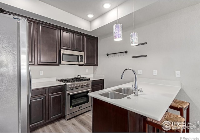 kitchen with a sink, light countertops, appliances with stainless steel finishes, hanging light fixtures, and a kitchen bar