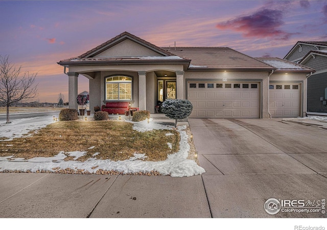 view of front of property featuring a garage, a tiled roof, concrete driveway, and stucco siding