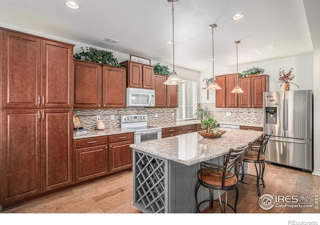 kitchen with visible vents, hanging light fixtures, light wood-style floors, a kitchen island, and white appliances