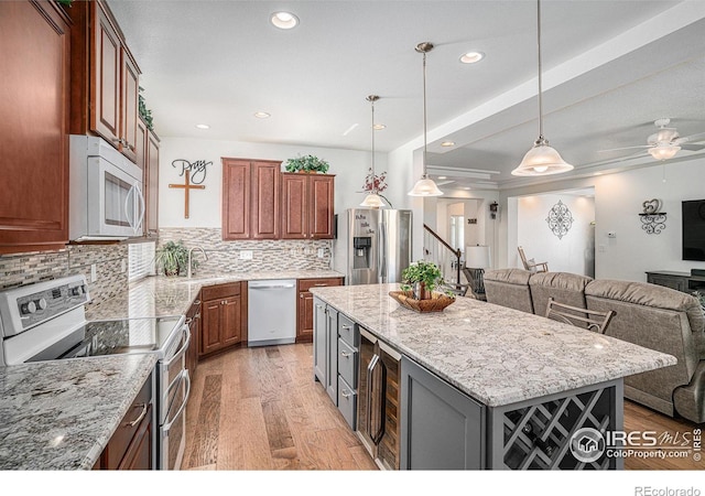 kitchen with appliances with stainless steel finishes, open floor plan, light stone counters, a center island, and hanging light fixtures