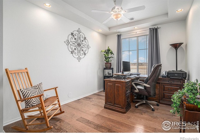 home office featuring ceiling fan, recessed lighting, baseboards, light wood-type flooring, and a tray ceiling