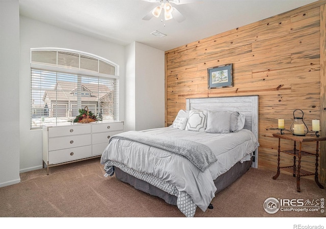 bedroom featuring carpet floors, ceiling fan, wooden walls, and visible vents