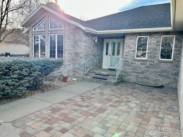 doorway to property featuring brick siding, roof with shingles, and a chimney