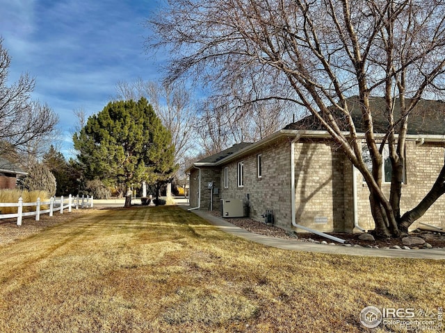 view of side of property with a yard, brick siding, central AC, and fence