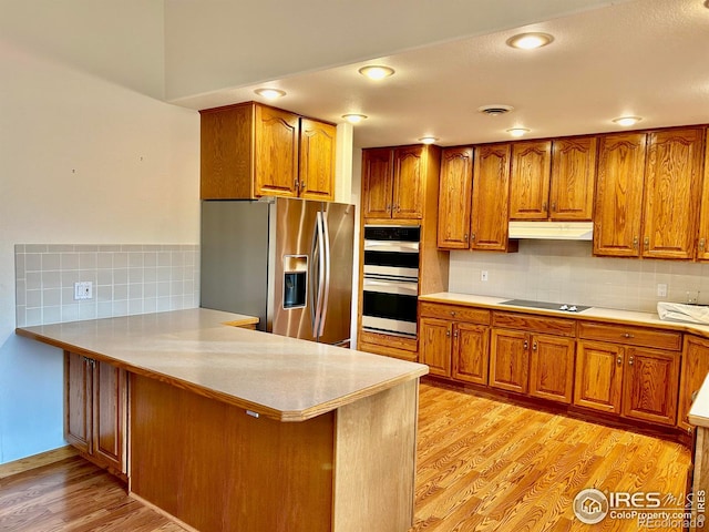 kitchen featuring under cabinet range hood, stainless steel appliances, light wood finished floors, and brown cabinetry