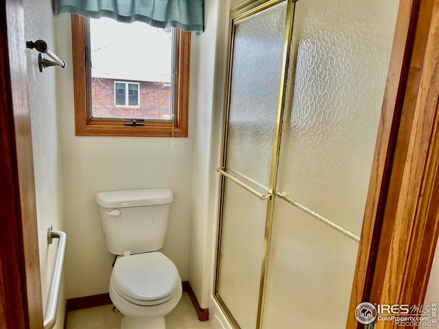 bathroom featuring a stall shower, toilet, and baseboards