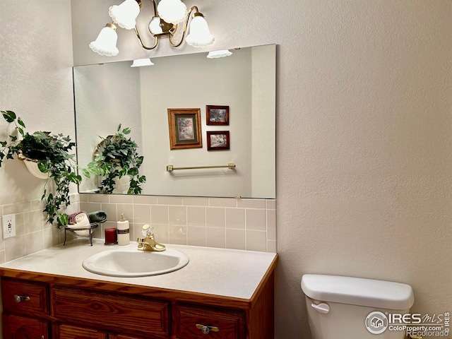 half bath featuring tasteful backsplash, a chandelier, vanity, and toilet