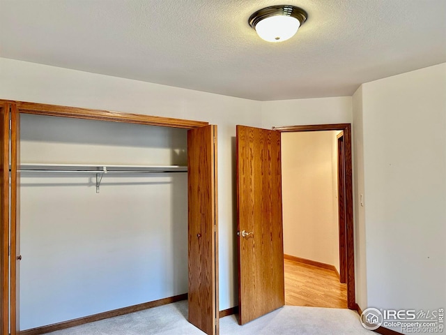 unfurnished bedroom with a textured ceiling, a closet, carpet, and baseboards