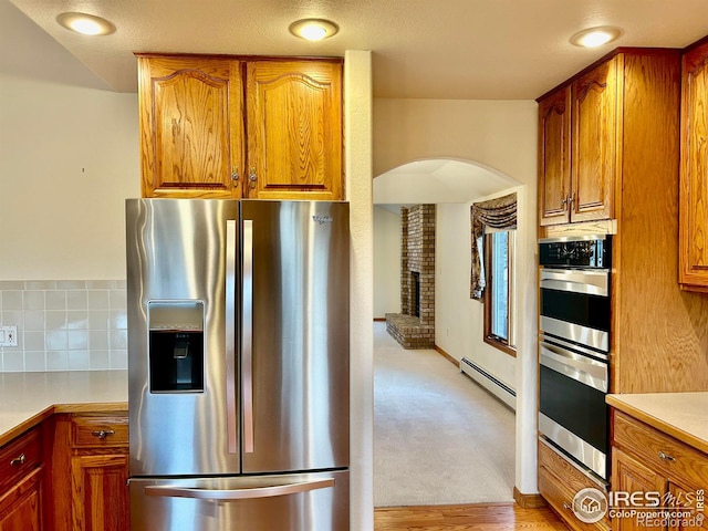 kitchen featuring tasteful backsplash, appliances with stainless steel finishes, brown cabinets, light countertops, and a baseboard heating unit