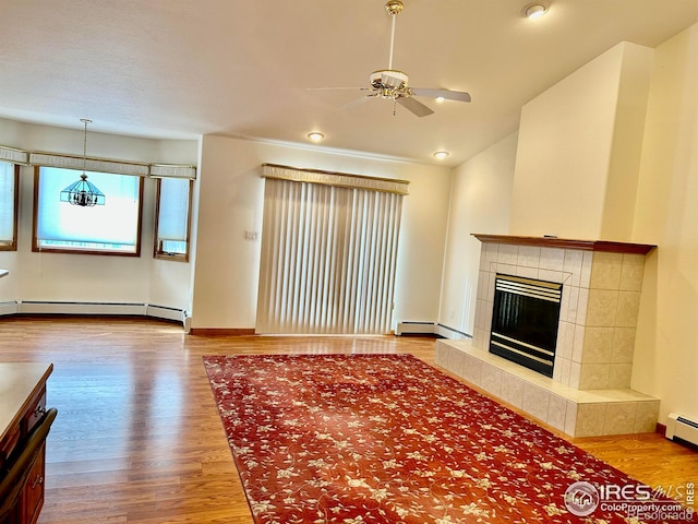 unfurnished living room featuring a baseboard heating unit, lofted ceiling, a tiled fireplace, and wood finished floors