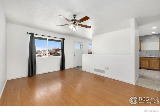 empty room featuring ceiling fan, light wood-style flooring, a sink, visible vents, and baseboards