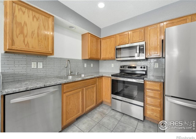 kitchen featuring tasteful backsplash, light stone counters, stainless steel appliances, a sink, and light tile patterned flooring