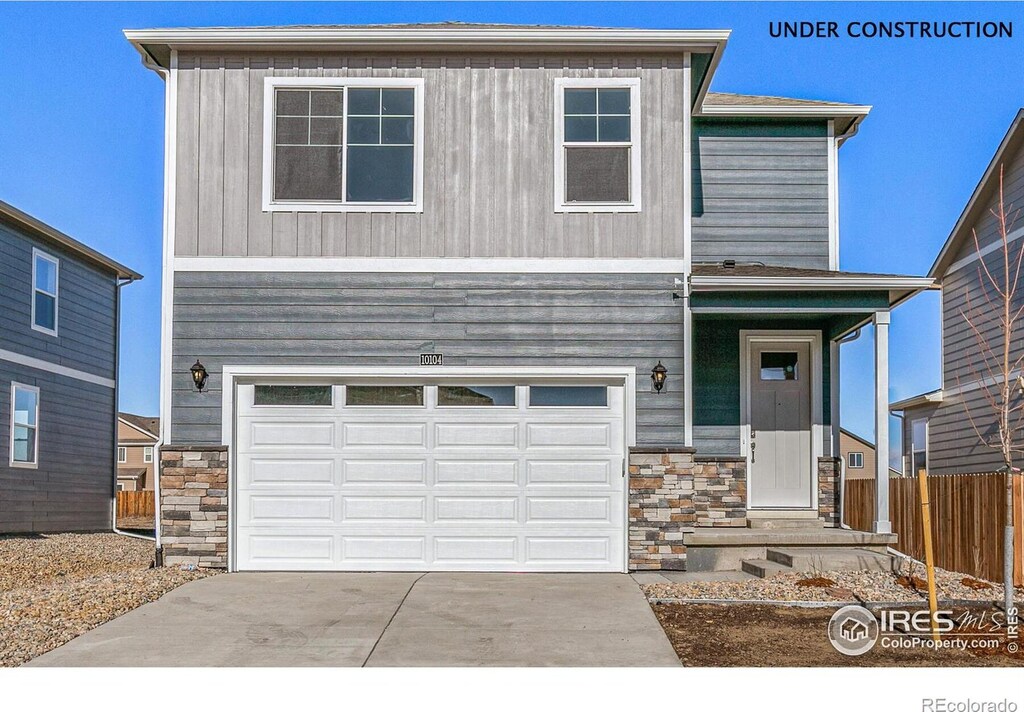 view of front of home featuring a garage, stone siding, driveway, and fence