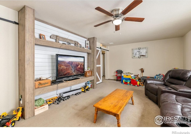 living area featuring carpet floors, a barn door, and ceiling fan