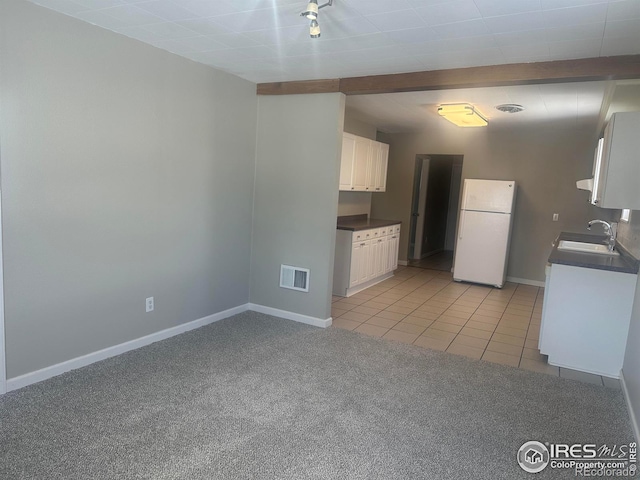 kitchen with dark countertops, freestanding refrigerator, light carpet, white cabinetry, and a sink