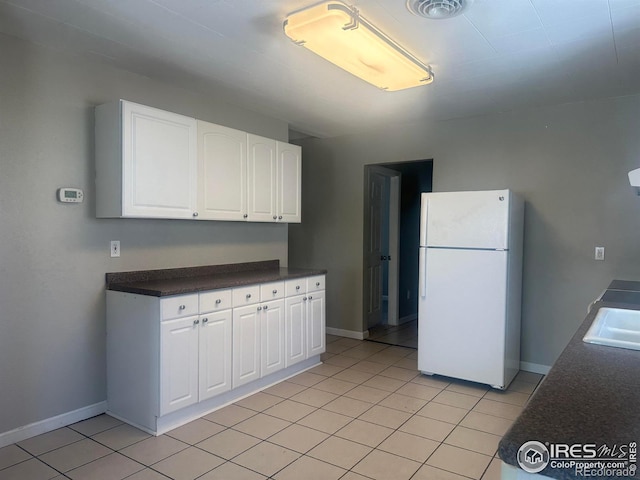 kitchen featuring light tile patterned floors, white cabinetry, baseboards, freestanding refrigerator, and dark countertops