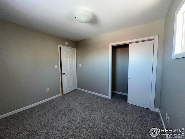 unfurnished bedroom featuring a closet, dark carpet, and baseboards