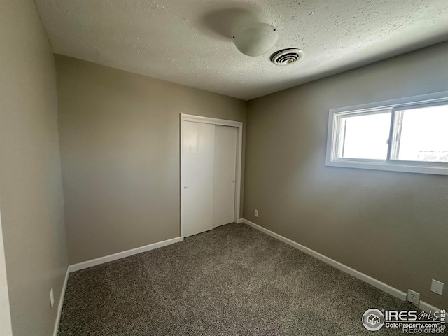 unfurnished bedroom featuring carpet floors, a closet, visible vents, a textured ceiling, and baseboards