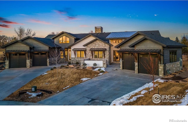 view of front of property with an attached garage, stone siding, driveway, and a chimney