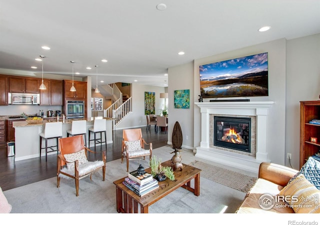 living area with light wood finished floors, baseboards, a glass covered fireplace, stairway, and recessed lighting