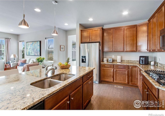 kitchen with dark wood finished floors, light stone counters, hanging light fixtures, stainless steel appliances, and a sink