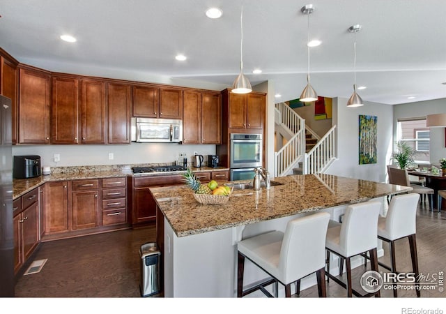 kitchen featuring stainless steel appliances, a breakfast bar, hanging light fixtures, dark wood finished floors, and a center island with sink