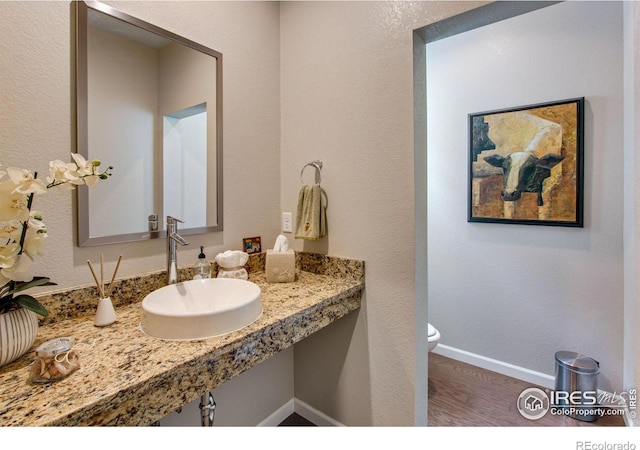 half bath featuring baseboards, a sink, toilet, and wood finished floors