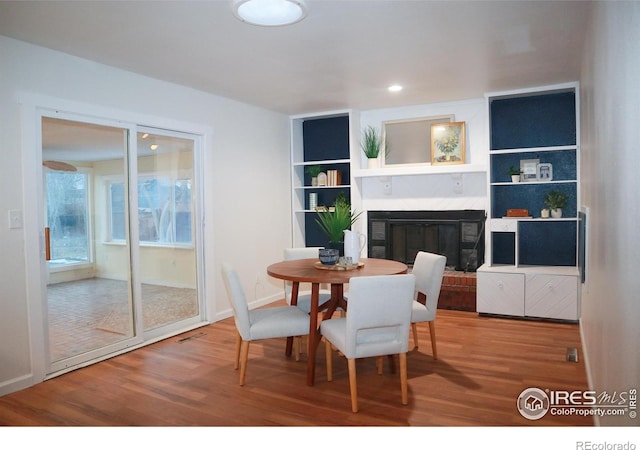 dining room with built in features, visible vents, wood finished floors, and a glass covered fireplace