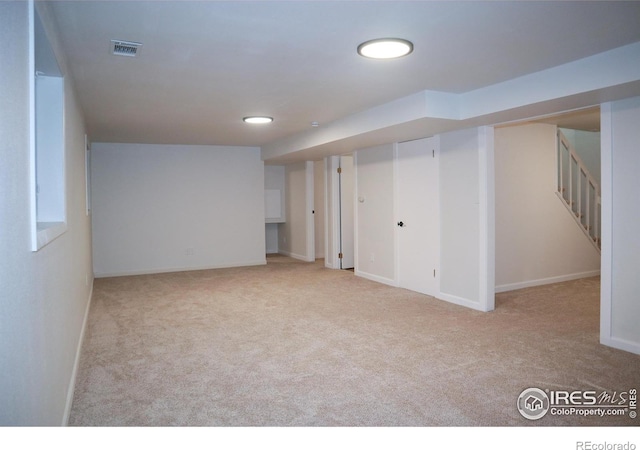 finished basement featuring light carpet, stairs, visible vents, and baseboards