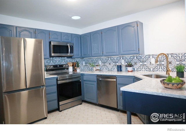 kitchen featuring appliances with stainless steel finishes, a sink, backsplash, and blue cabinetry