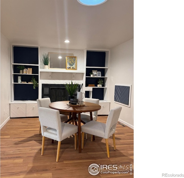 dining area with built in shelves, baseboards, wood finished floors, and a glass covered fireplace