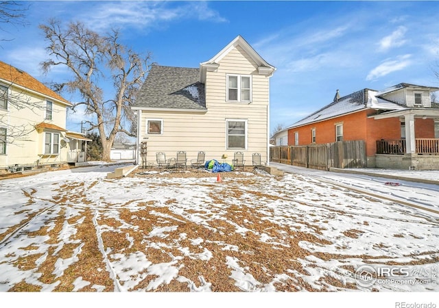 snow covered property with roof with shingles and fence