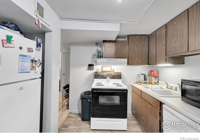 kitchen with white appliances, light wood-style floors, light countertops, under cabinet range hood, and a sink