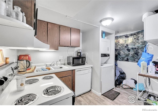 kitchen featuring stacked washer and clothes dryer, light countertops, light wood-style flooring, a sink, and white appliances