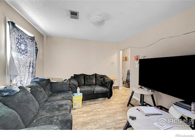 living room featuring a textured ceiling, light wood finished floors, and visible vents