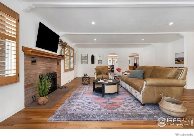 living room with a warm lit fireplace, arched walkways, and wood finished floors