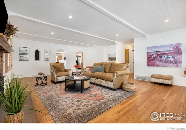 living area featuring arched walkways, recessed lighting, visible vents, light wood-type flooring, and beam ceiling