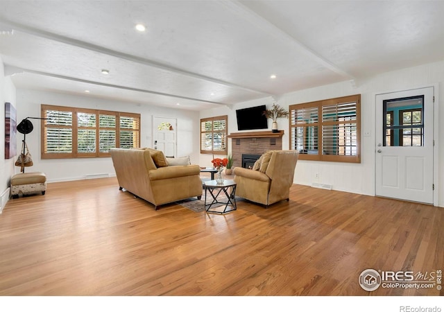 living room featuring a fireplace, visible vents, baseboards, beam ceiling, and light wood finished floors