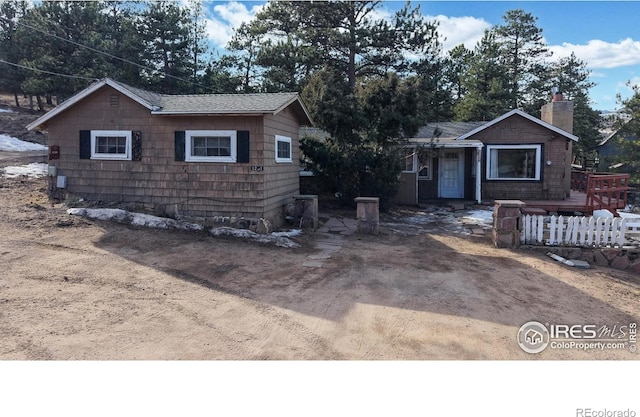 view of front of house with driveway, a shingled roof, a chimney, and fence