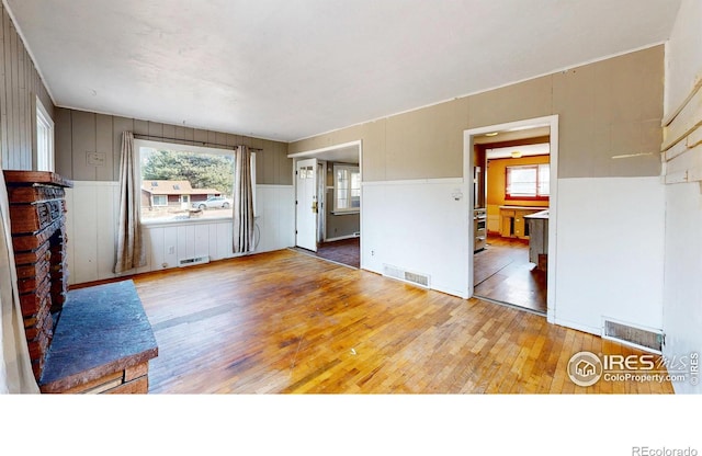 unfurnished living room featuring a wealth of natural light, a brick fireplace, visible vents, and wood finished floors