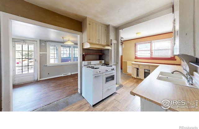 kitchen featuring under cabinet range hood, a sink, light wood-style floors, light countertops, and white gas range