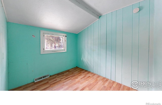 spare room with wooden walls, visible vents, vaulted ceiling with beams, and light wood-style flooring