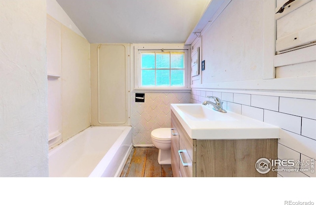 bathroom featuring lofted ceiling, toilet, tile walls, vanity, and a bathtub